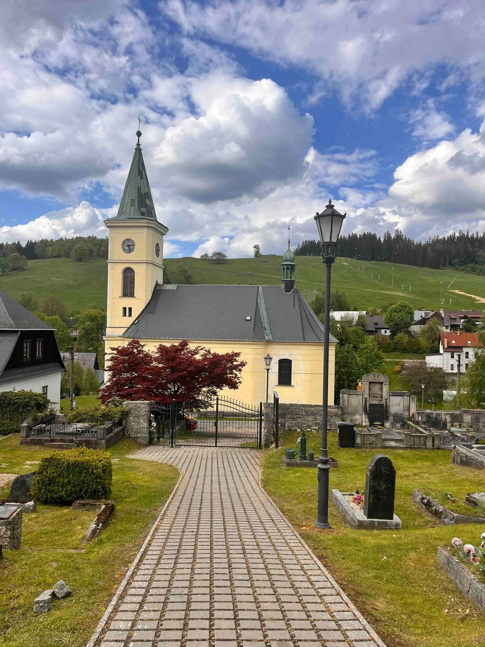 Kostel a hřbitov v Albrechticích, v pozadí zalesněný vrch